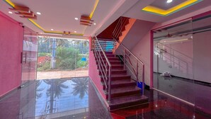Un interior moderno con un ascensor de vidrio, una escalera con barandillas metálicas y vistas al exterior con vegetación.