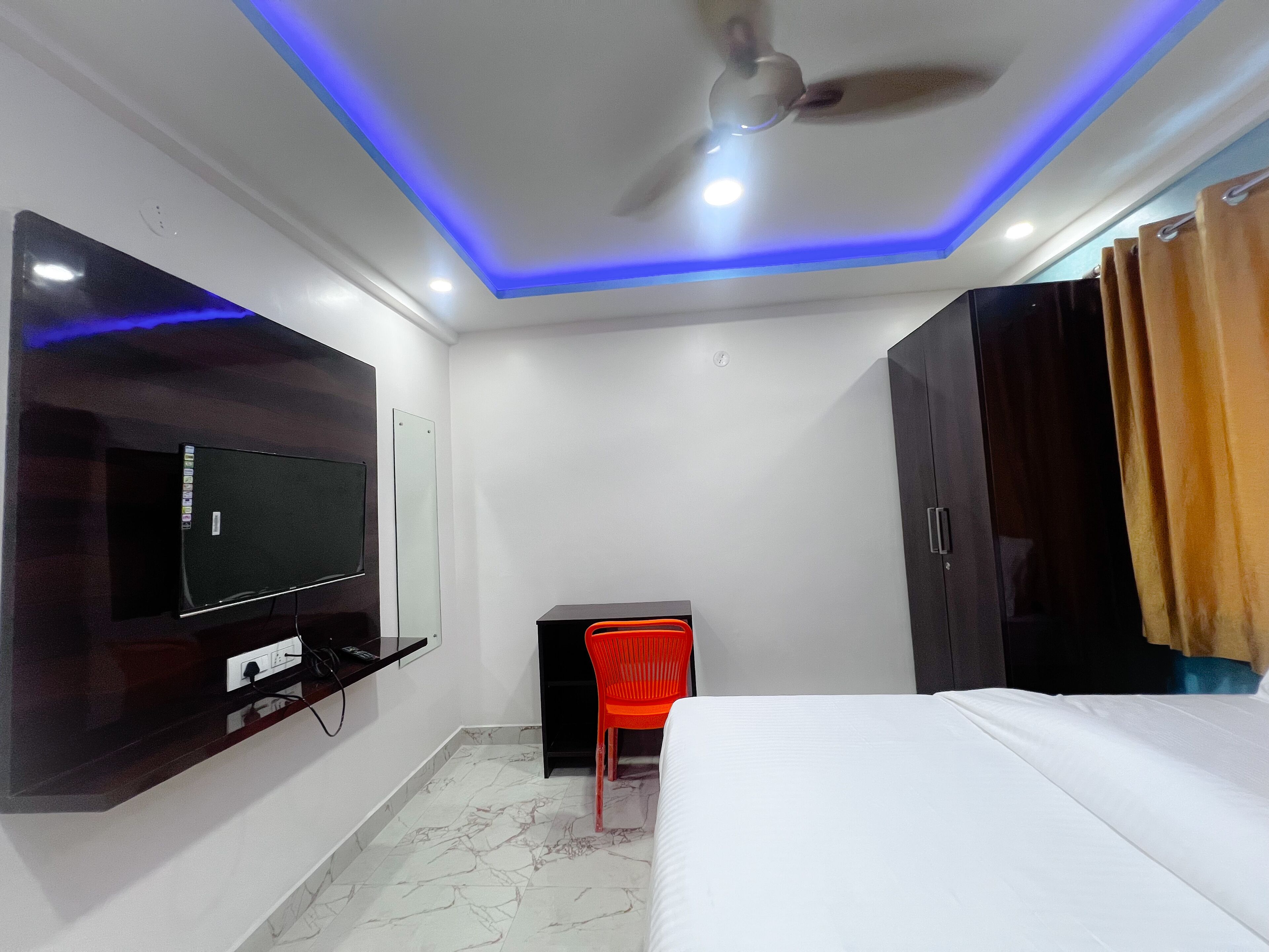 A hotel room with a bed, a TV mounted on the wall, a desk with a chair, and a ceiling fan.