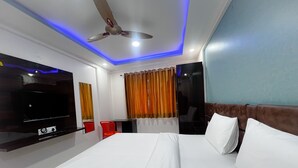 Una habitación de hotel con cama, televisión, ventilador de techo y ventana con cortinas.