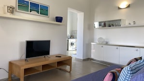 Ein modernes Wohnzimmer mit Fernseher, einer Holzbank und einem Sofa. Es gibt eine Waschküche mit Waschmaschine und Spüle.