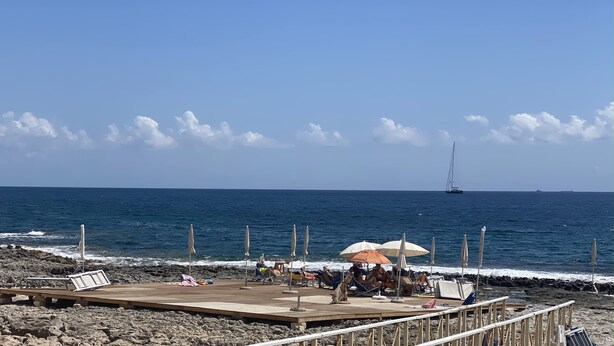 Ein Strand mit einer Holzsteg, Sonnenschirmen und Liegestühlen.