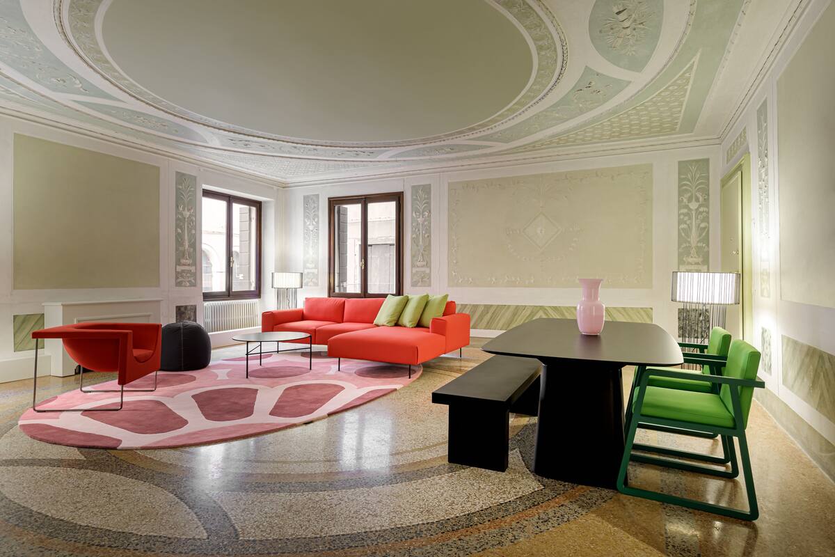 Una sala de estar moderna con un sofá rojo, sillas verdes, una mesa negra y una alfombra rosa.