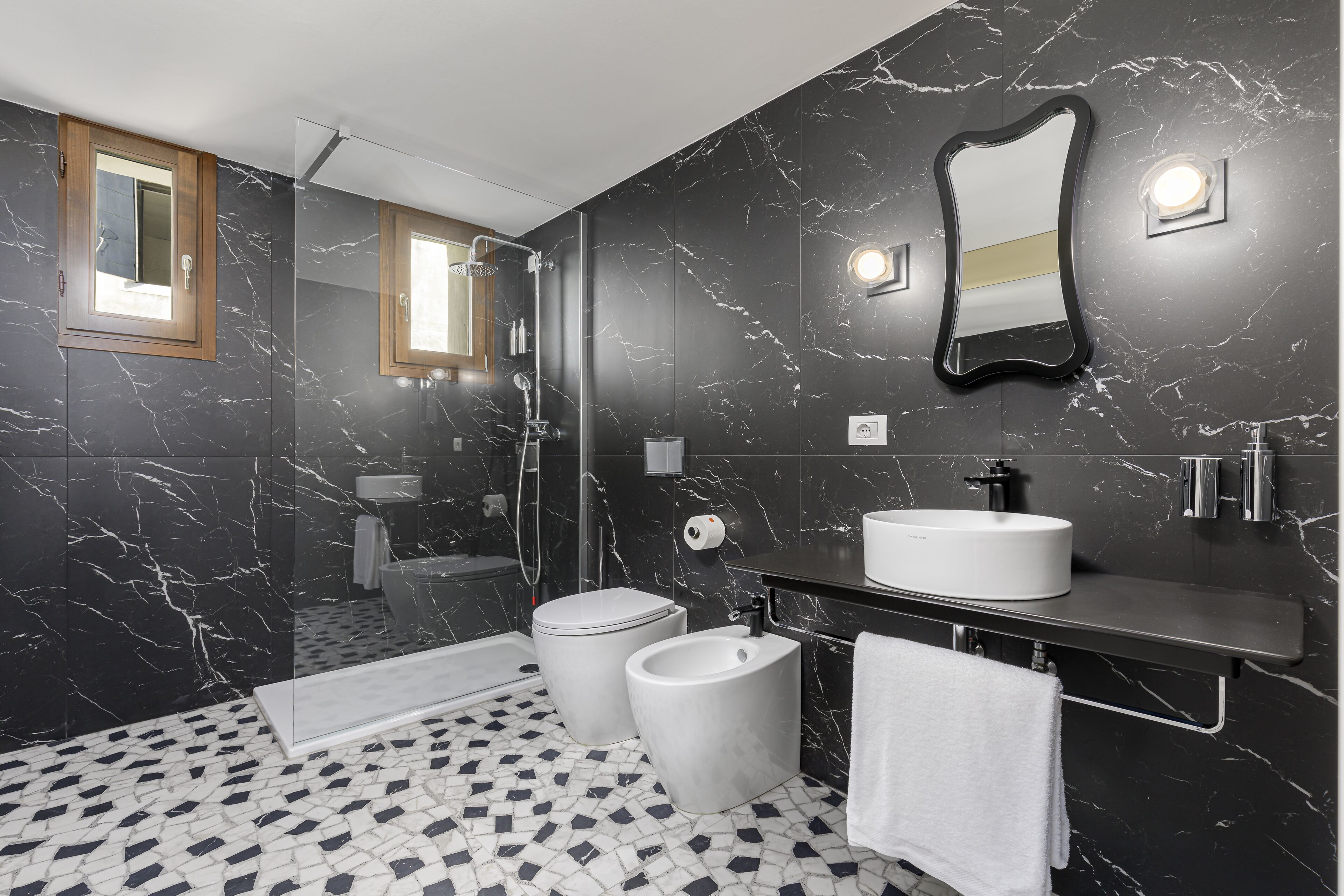 Un bany modern amb una paret de marbre negre, un lavabo blanc, un mirall i una zona de dutxa.