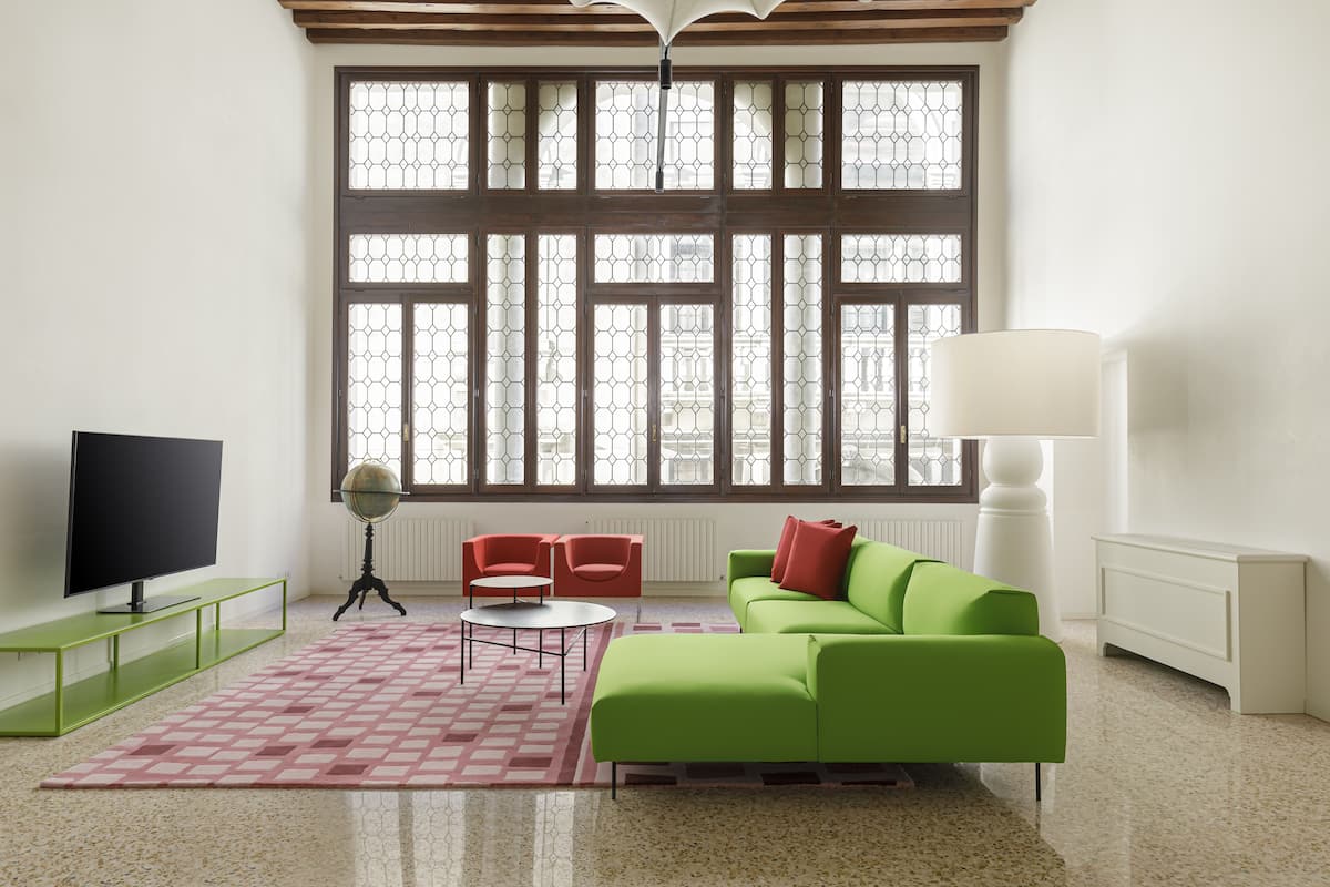 Una sala moderna con un sofá verde, sillas rojas, un televisor y ventanas amplias.