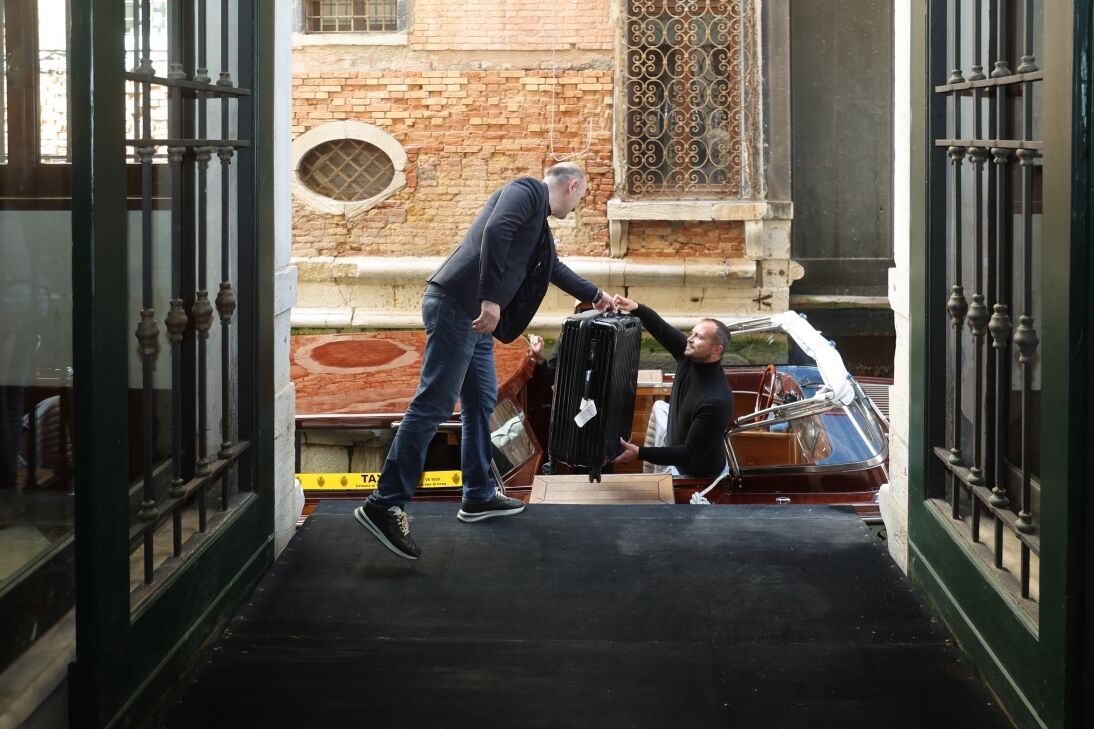 A man and a woman in a narrow alleyway, with a vintage car parked on the side.
