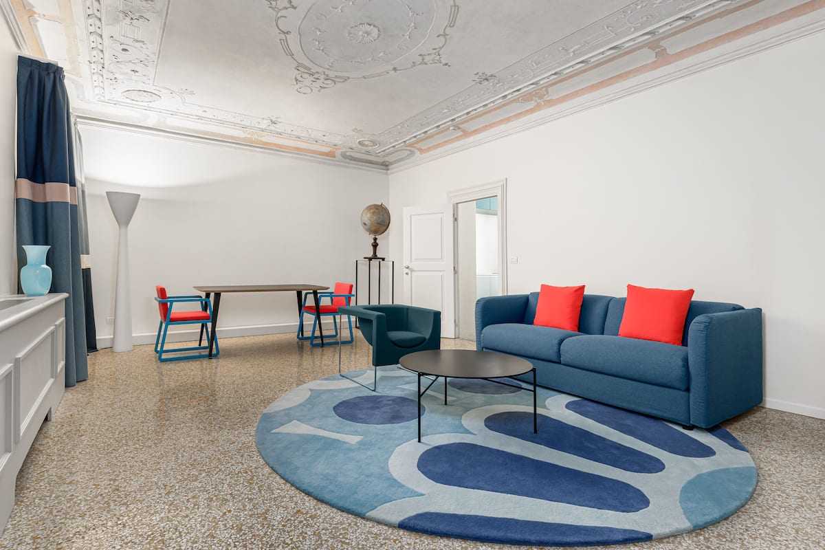Una sala de estar moderna con un sofá azul, cojines rojos, una mesa de centro redonda y un globo terráqueo sobre un atril.