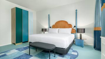 Quarto de hotel moderno com uma cama grande, um banco, duas mesas de cabeceira e um guarda-roupa.