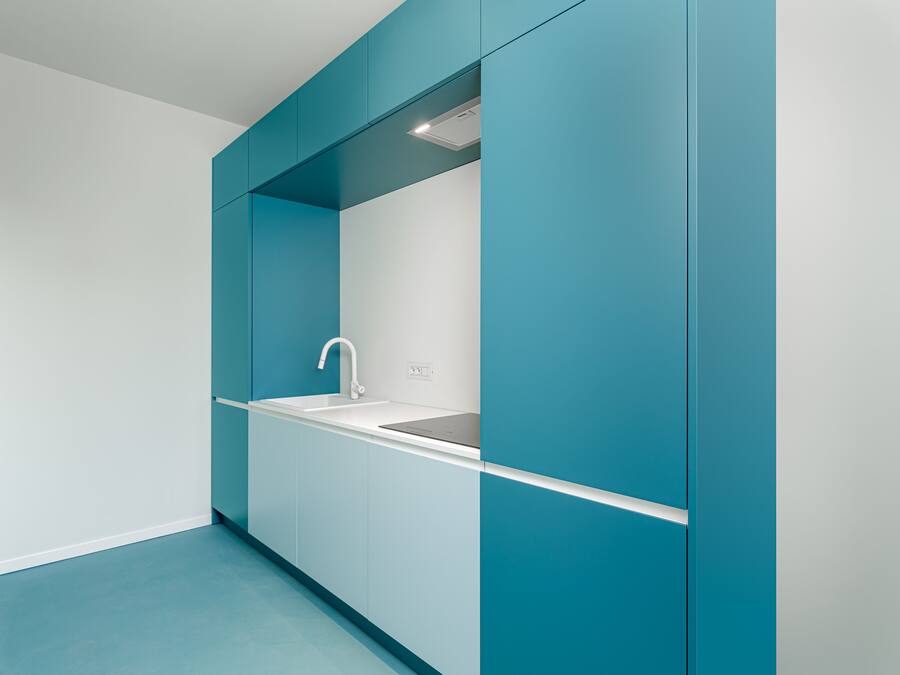 A modern kitchen with teal cabinetry, a white countertop, and a built-in sink.