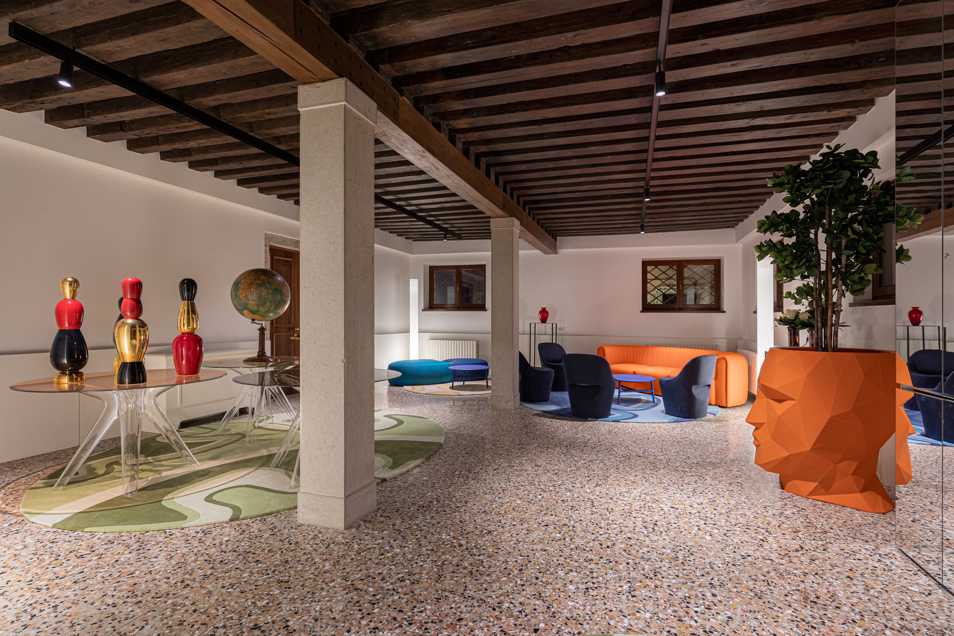 A modern interior with a high ceiling, exposed beams, and a mix of seating areas including sofas and chairs.