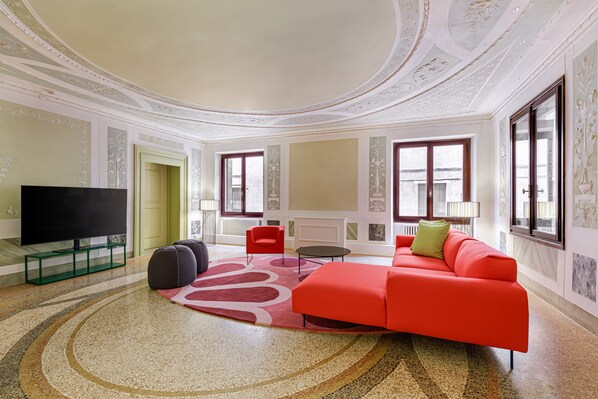 Un salon spacieux doté d’un grand téléviseur à écran plat, d’un canapé rouge et d’un tapis à motifs.