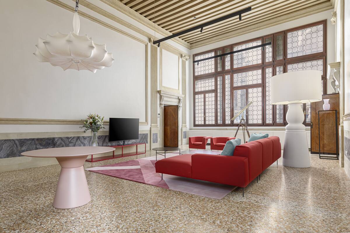 Una sala de estar moderna con un sofá rojo, una mesa rosa y un ventanal con vidrios decorativos.