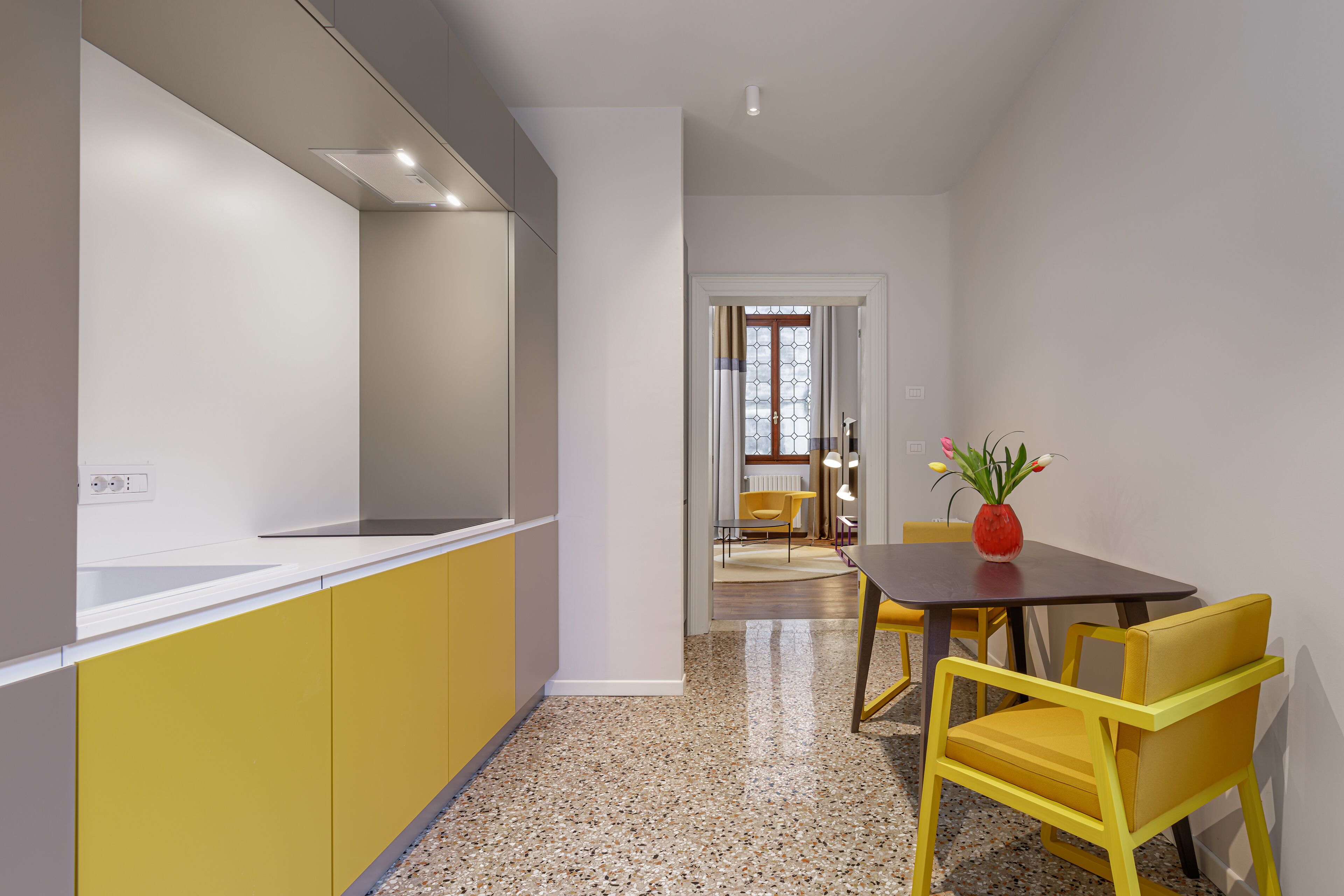 Una cocina moderna con armarios amarillos, encimera blanca y un comedor con sillas y mesa amarillas.