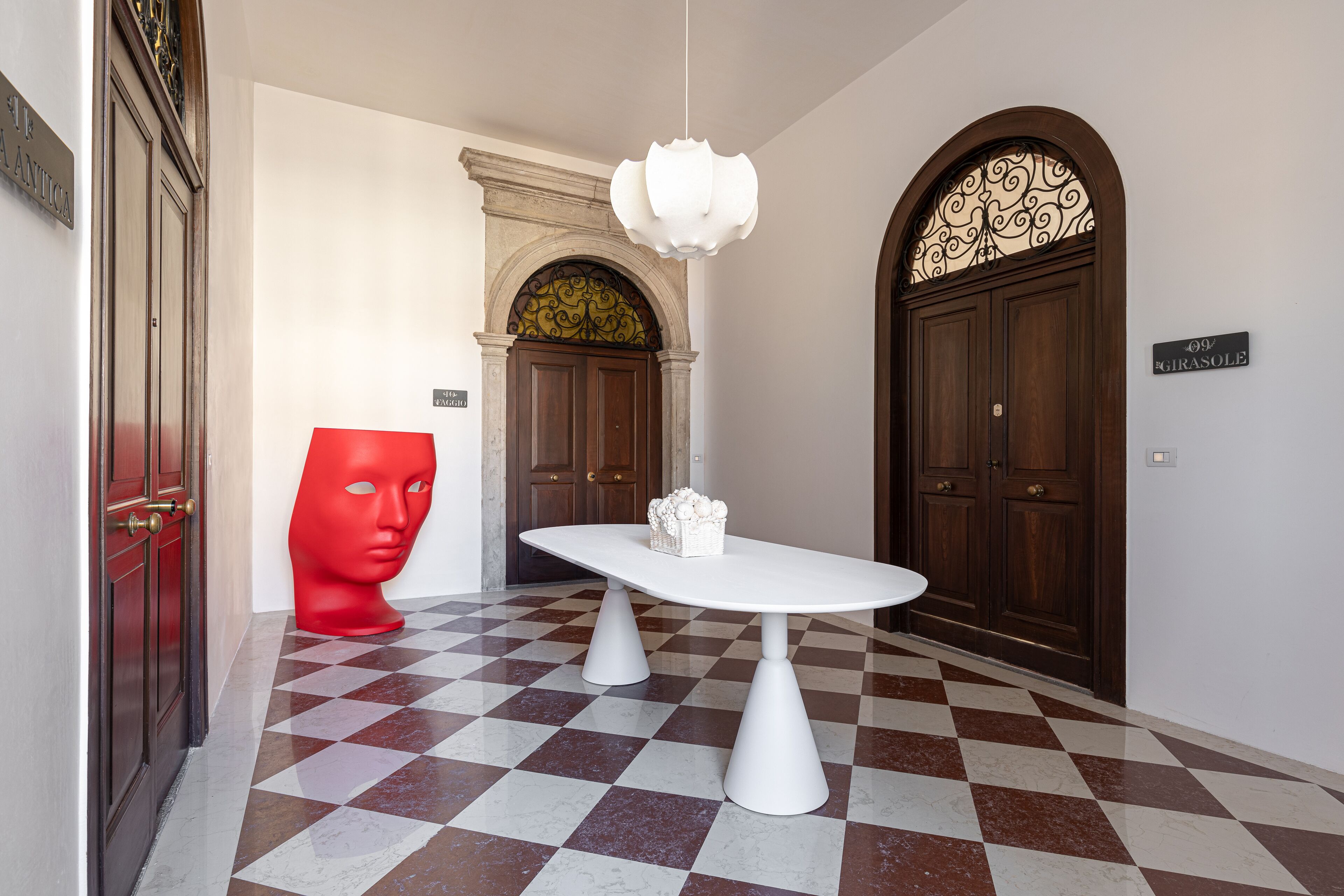 Un suelo a cuadros, una mesa blanca con un objeto decorativo y dos puertas de madera con un cartel sobre una de ellas.