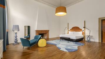 Un dormitorio moderno con cama, una silla azul, un reposapiés amarillo, chimenea y lámpara colgante.