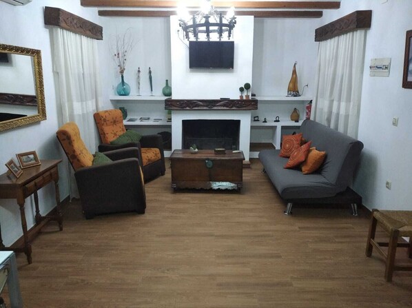 Una sala de estar con chimenea, un sofá, una silla, una mesa de centro y un televisor sobre la chimenea.