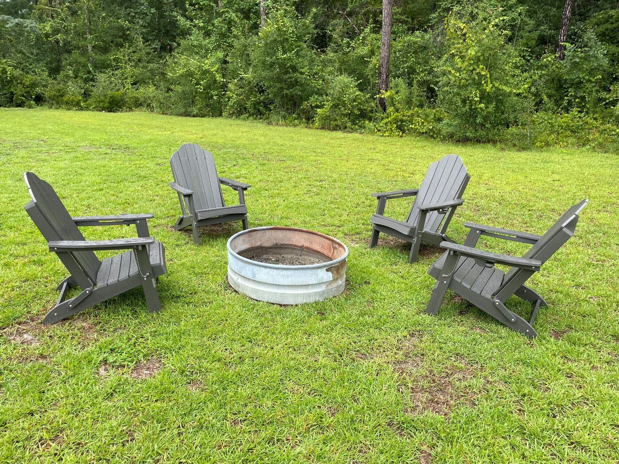 A circular fire pit with four Adirondack chairs arranged around it on a grassy lawn.