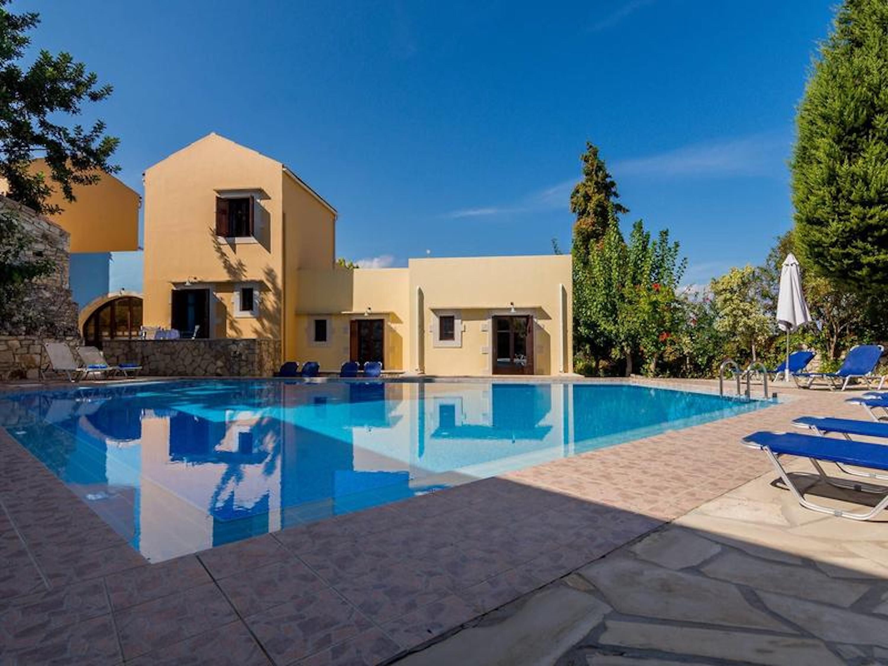 Una piscina con lettini e un edificio con diverse porte e finestre.