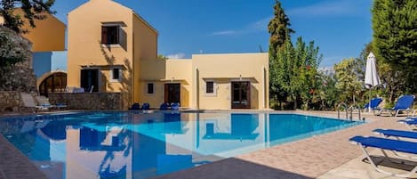 Una piscina con sillas de descanso y un edificio con varias puertas y ventanas.