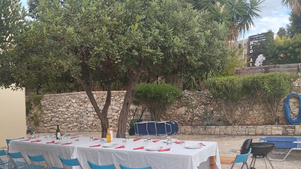 An outdoor dining area with tables set for four, blue chairs, and a stone wall in the background. - Group Accommodation in Crete Separate Houses (Apokoronas)