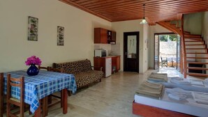 A cozy room with a sofa, a dining table with a checkered tablecloth, a kitchen area, and a staircase leading to another level. - Group Accommodation in Crete Separate Houses (Apokoronas)