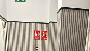 Un couloir aux murs rayés, un extincteur fixé au mur et des panneaux indiquant les sorties de secours.