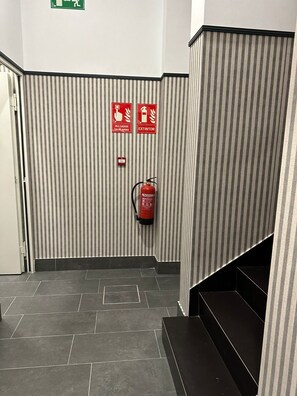 Een gang met gestreepte muren, een aan de muur bevestigde brandblusser en nooduitgangsborden.