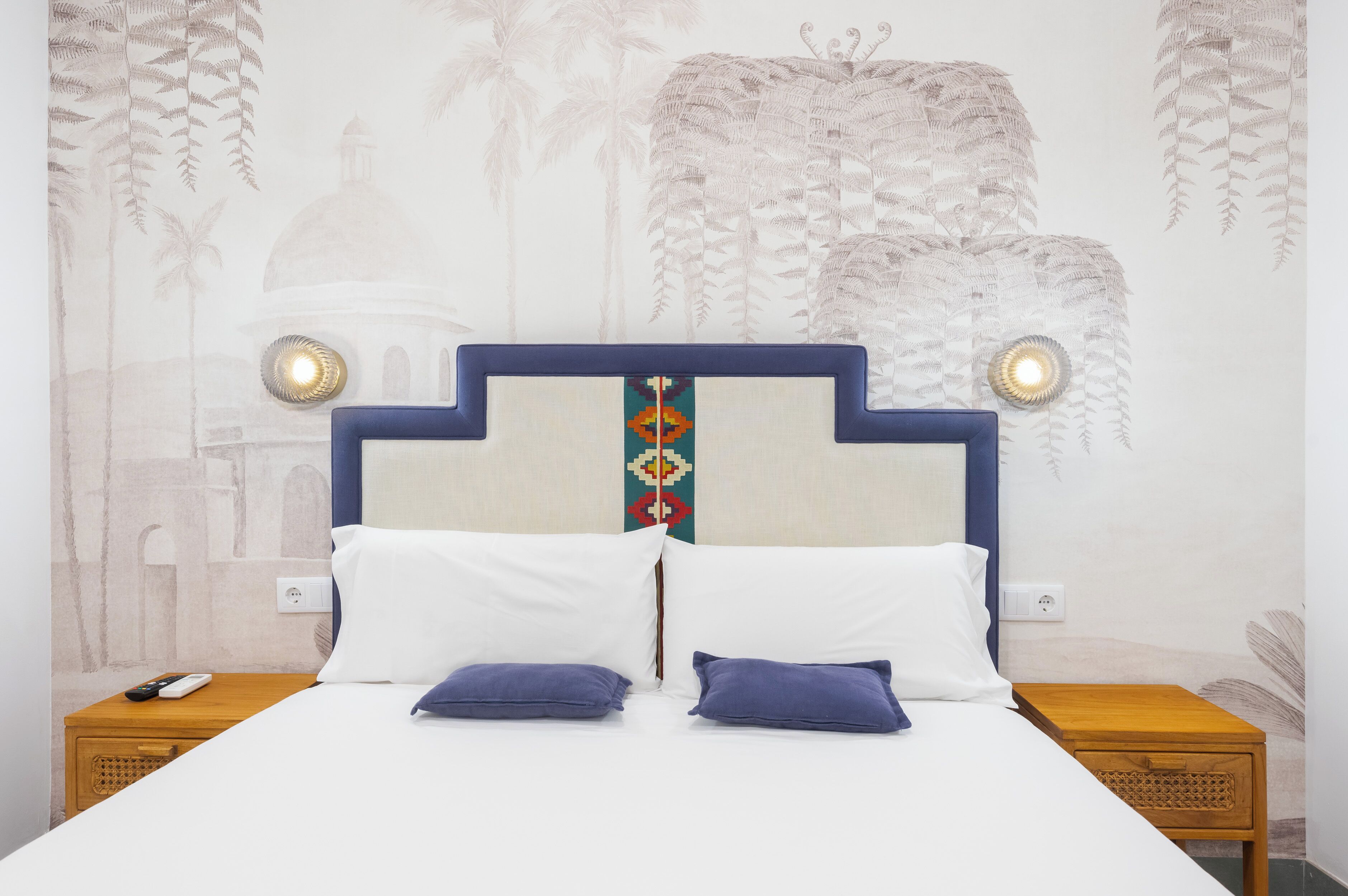 A bed with a headboard, two bedside tables, and a wall with a mural.