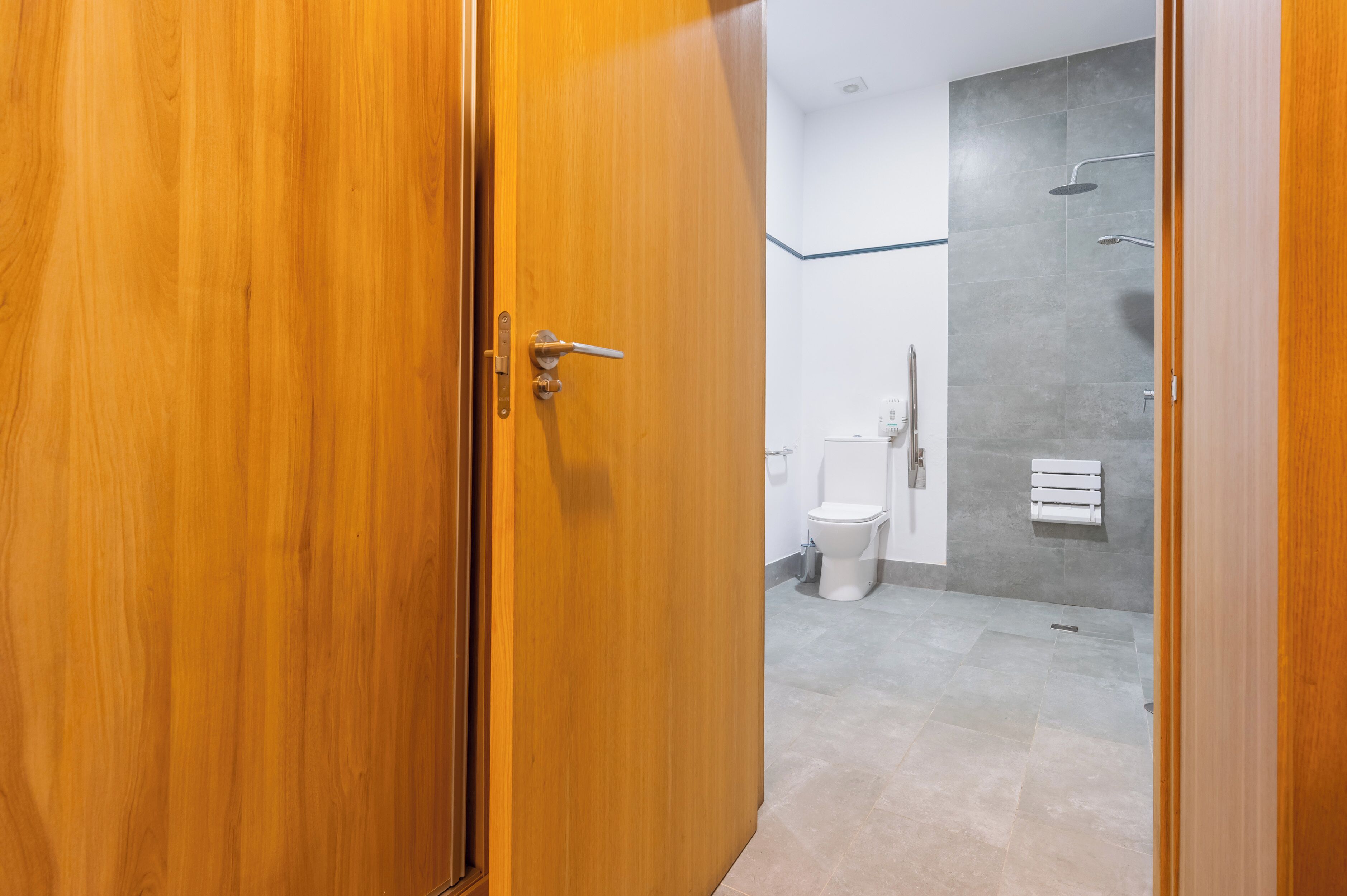 Une porte en bois donne accès à une salle de bain équipée de toilettes, d’une douche et d’un porte-serviettes.