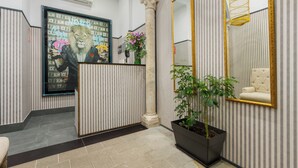 Zona de recepción con pared a rayas, una obra de arte grande enmarco, una planta en maceta y un espejo con marco dorado.