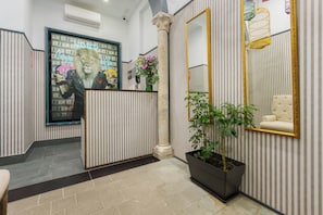 Een receptiegedeelte met een gestreepte muur, een groot ingelijst kunstwerk, een potplant en een spiegel met gouden lijst.
