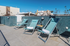 Zona de piscina en la azotea con sillones reclinables y una mesa con una botella y vasos.