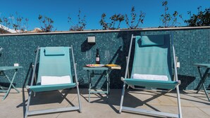 Dos sillones de descanso con toallas, una mesa con una botella de vino y un muro de azulejos al fondo.