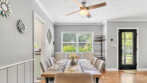 A dining room with a wooden table, beige chairs, a ceiling fan, and a window with blinds.