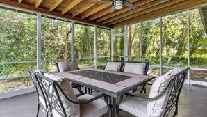 A covered outdoor dining area with a table and chairs, large windows, and a ceiling fan.