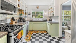 A kitchen with white cabinets, a black and white checkered floor, a gas stove, and a window with a view of greenery.