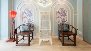 A room with two wooden chairs, a red floor lamp, and a white birdcage with pink branches. - Sino Siam Hotel (Krabi)