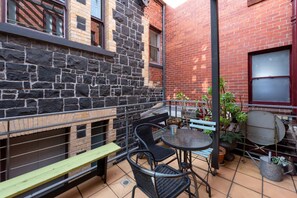 A small outdoor patio with a stone wall, a metal railing, a round table, and several chairs. - Bright & Sunny 2-bed Unit in the Heart of St Kilda (St Kilda)