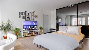 A modern bedroom with a bed, a TV, a bookshelf, and a large mirror. - Design Apartment in the City Center and Garage (Hameenlinna)
