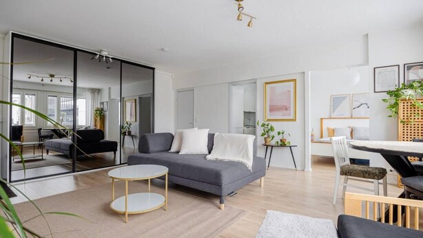 A modern living room with a grey sofa, a round coffee table, and a dining area with a white table and chairs. - Design Apartment in the City Center and Garage (Hameenlinna)