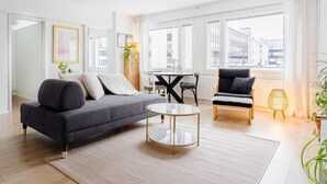 A modern living room with a grey sofa, a round coffee table, and a black armchair. There is a dining table with chairs and a window with curtains. - Design Apartment in the City Center and Garage (Hameenlinna)