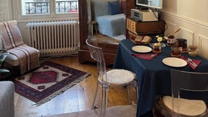 A cozy room with a wooden bed, a dining table set for two, a chair, a radiator, and a window with a view of the outside. - Appart aux Gobelins à 15 min à Pied de Saint Michel, Notre Damme et Montparnasse (Paris)