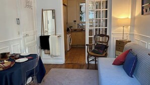 A room with a bed, a chair, a table, and a mirror. There is a door leading to another room with a washing machine. - Appart aux Gobelins à 15 min à Pied de Saint Michel, Notre Damme et Montparnasse (Paris)