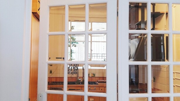A white door with multiple glass panels leading to a kitchen area with wooden cabinets and a tiled floor. - Appart aux Gobelins à 15 min à Pied de Saint Michel, Notre Damme et Montparnasse (Paris)
