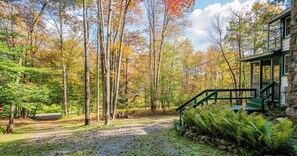 A stone house with a green staircase leading to a porch, surrounded by a forest with autumn foliage.