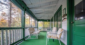 A covered porch with green walls and white railings, featuring several wicker chairs and a hammock.