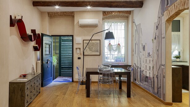 Un pasillo con suelo de madera, una puerta azul, un mapa en la pared y una ventana con vistas a edificios.