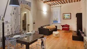 Una sala de estar con comedor, piso de madera, un sillón rojo, un sofá y un cuadro en la pared.