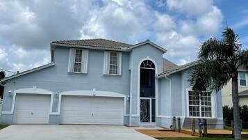 Two-story home with a decorative archway and garage, set amidst a well-manicured lawn and a palm tree.