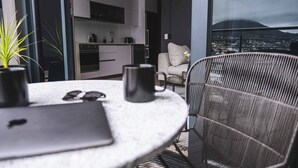 Eine moderne Küche mit weißen Schränken, ein Essbereich mit rundem Tisch und Blick auf eine Stadtlandschaft durch große Fenster.