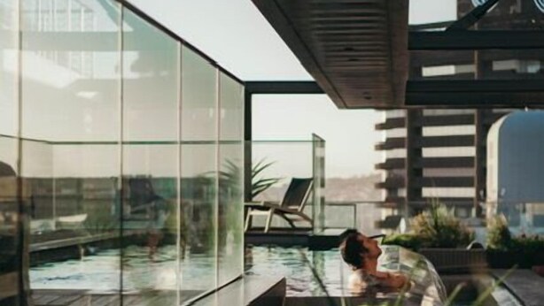 Ein moderner Poolbereich im Freien mit Glaswänden, Liegestühlen und Pflanzen in Kübeln.